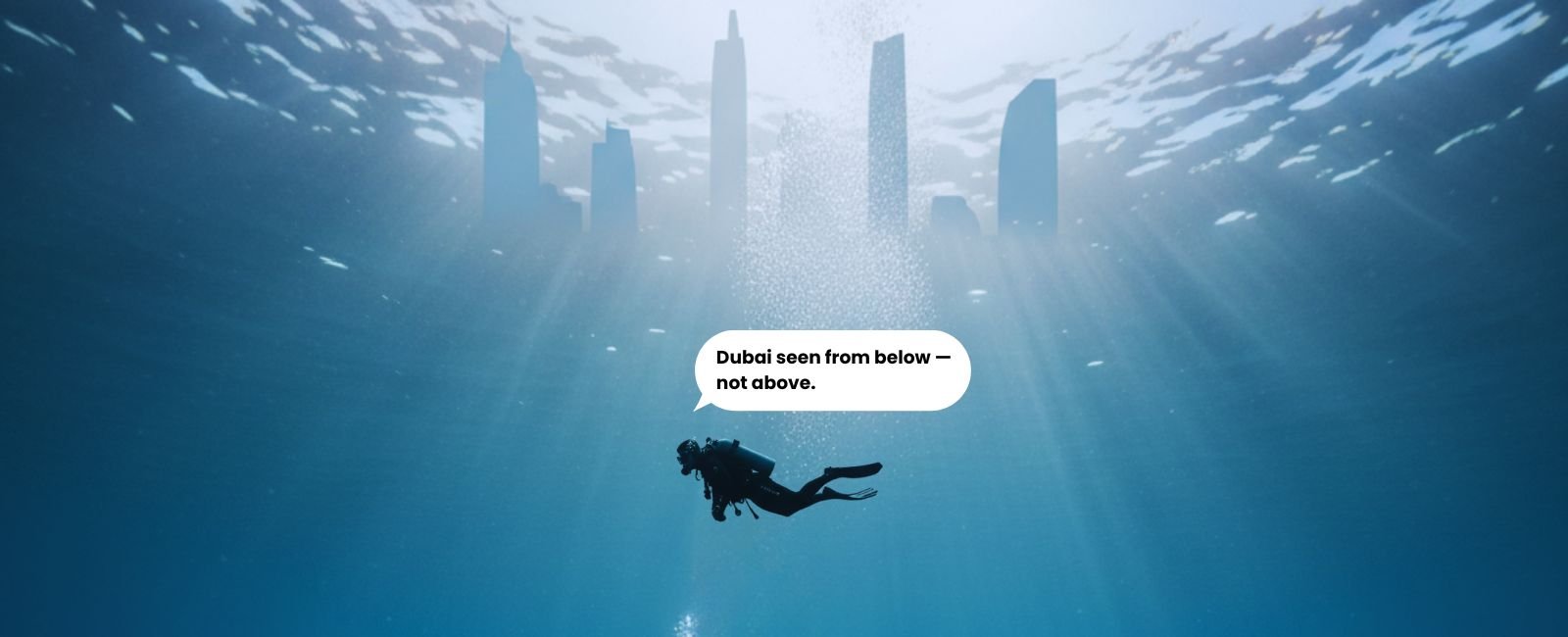 A single scuba diver floating calmly beneath the surface in Dubai, sunlight filtering through blue water as the city fades into silence below.